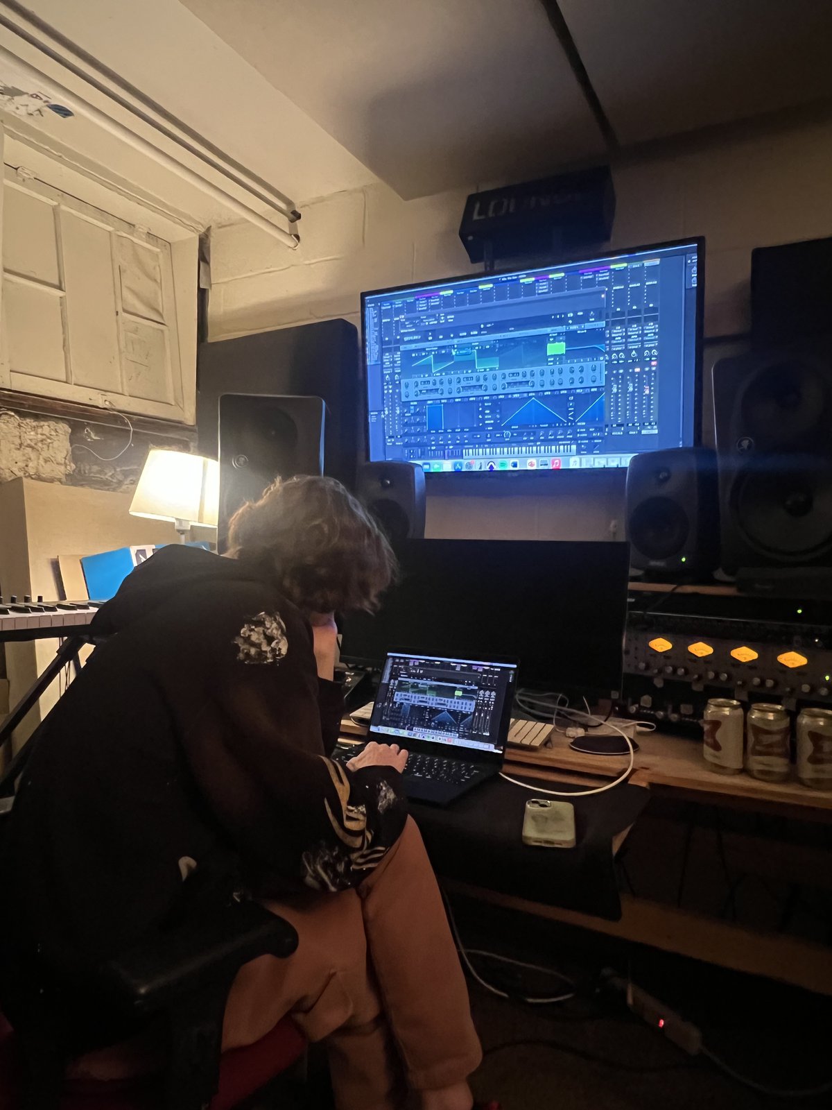 Ezra at a home studio desk, working at a laptop under a wall of monitors and outboard gear.